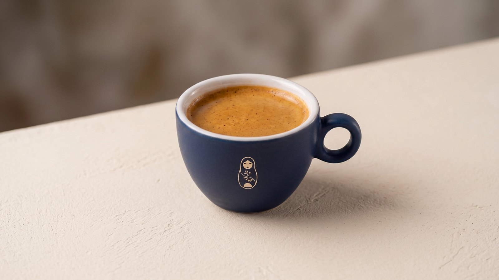 Espresso in a matte navy ceramic cup on a warm off-white surface at Krasivo Beauty Cafe, Upper East Side